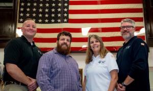 Four people posing in front of American flag.